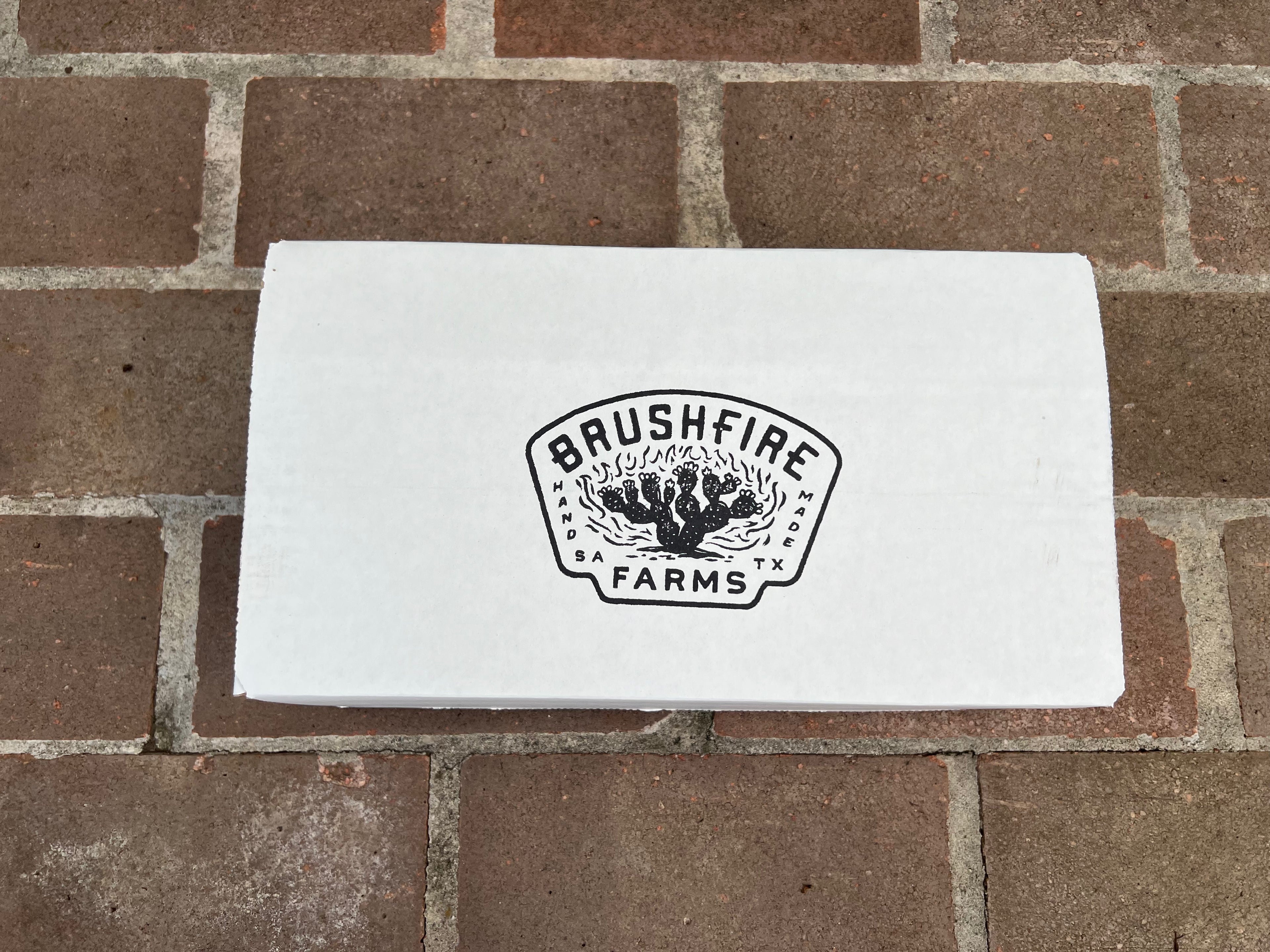 White box with Brushfire Farms logo on a brick surface, showcasing the Three Amigos product.