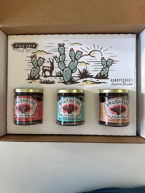 Three jars of Brushfire Farms pepper jams in a gift box, featuring colorful labels and a hand-drawn cactus design.