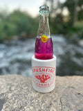 Brushfire Farms boat koozie holding a colorful beverage by a river, showcasing the brand's logo prominently.