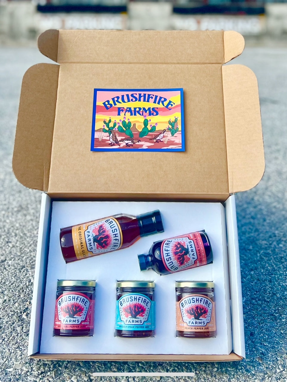 Gift box featuring Brushfire Farms' El Jefe products, including pepper jams and prickly pear syrup, arranged attractively.