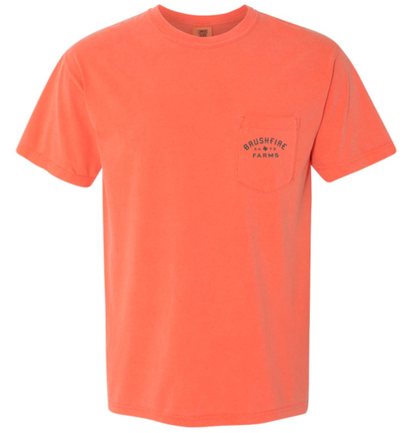 Salmon-colored t-shirt featuring a pocket with the Brushfire Farms logo and cactus design. Ideal for casual wear.