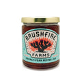 Jar of Brushfire Farms Prickly Pear Pepper Jam featuring a colorful label with a cactus design and gold lid.
