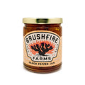 Jar of Brushfire Farms Peach Pepper Jam featuring a colorful label with cacti and flames, showcasing its handmade quality.