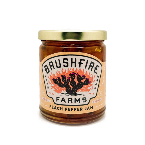 Jar of Brushfire Farms Peach Pepper Jam featuring a colorful label with cacti and flames, showcasing its handmade quality.