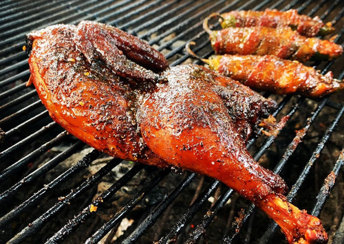 Grilled chicken coated in Brushfire Glaze, with stuffed jalapeños in the background, showcasing a smoky, flavorful finish.